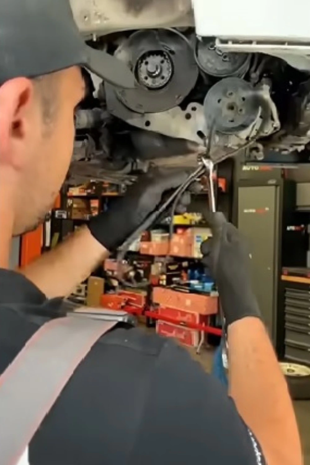 A mechanic working under a lifted car, using a wrench on a component.